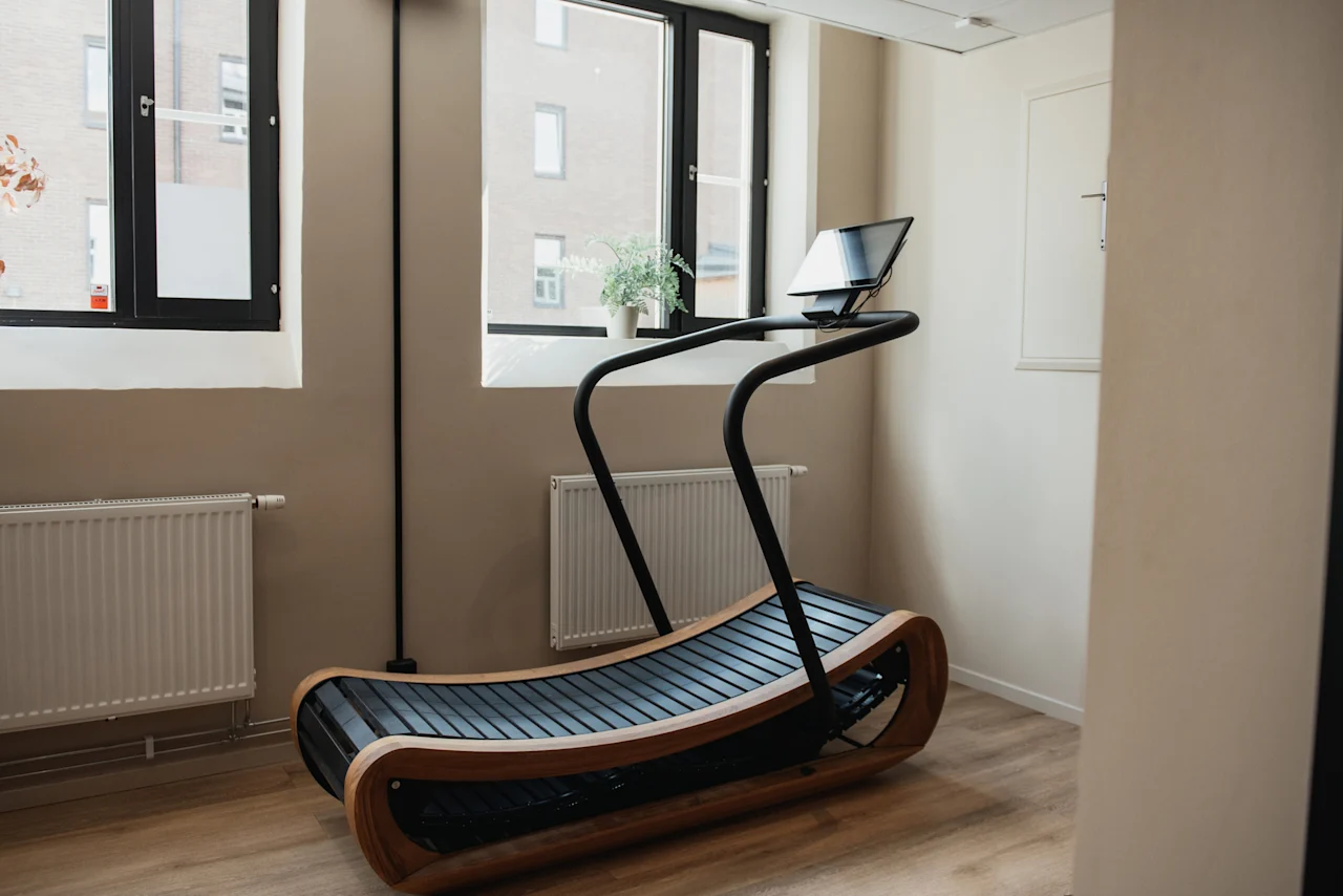 A modern treadmill with a sleek design in a bright room with windows, offering a pleasant workout experience at Home Hotel Uppsala.
