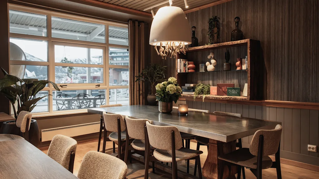 An elegant dining or meeting room featuring a long wooden table, comfortable chairs, and a large window overlooking a scenic view.
