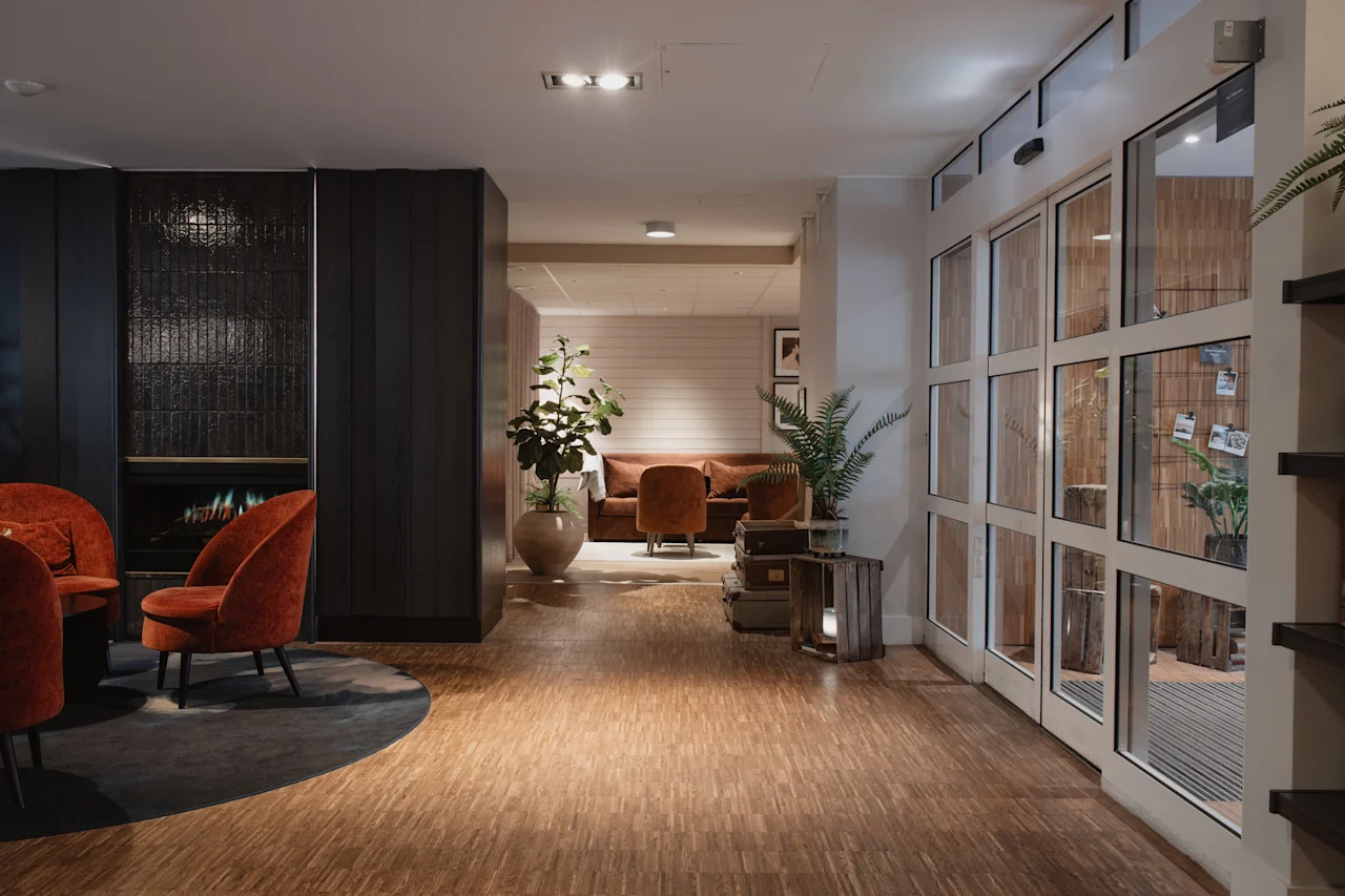 Et varmt og indbydende hotelloungeområde med komfortable siddepladser, en pejs og store glasdøre, der fører til et andet rum.