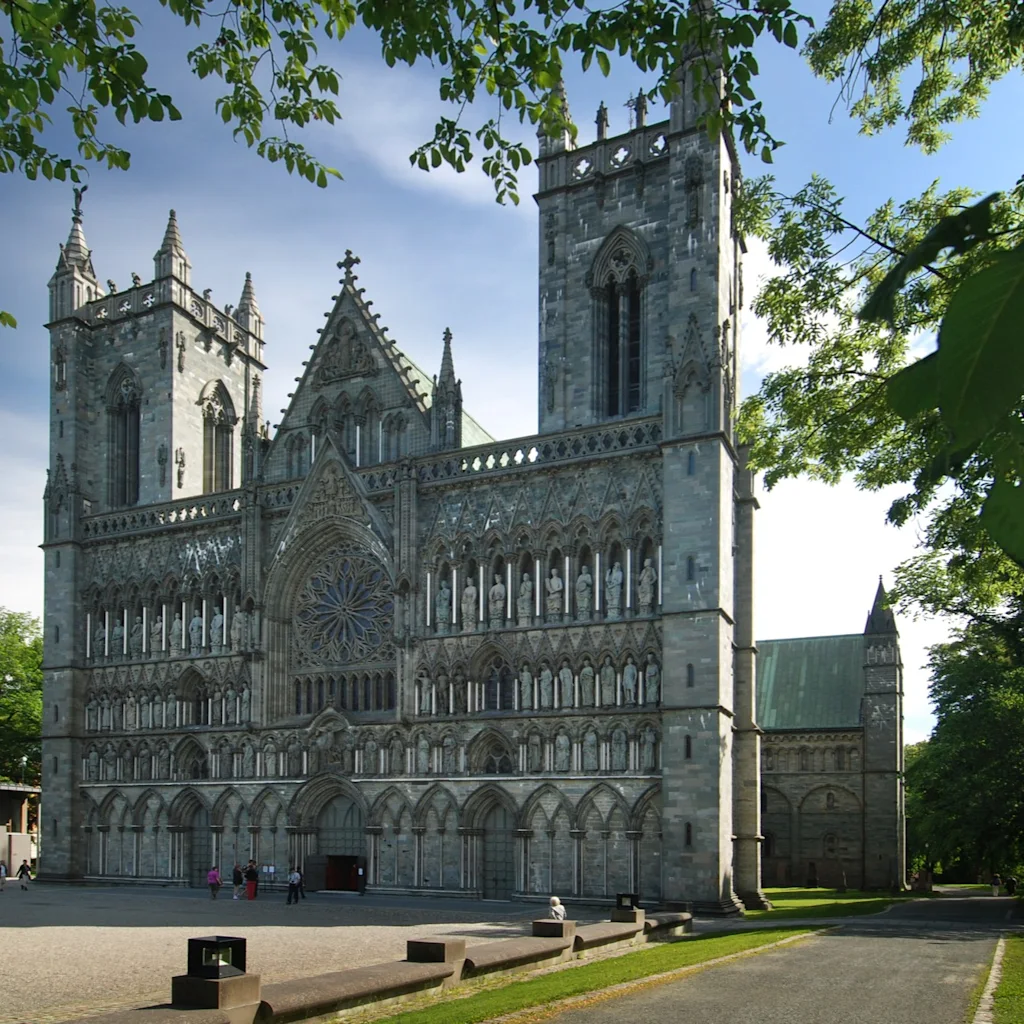 Upea kivikatedraali, jossa on kaksi suurta tornia ja yksityiskohtainen julkisivu, sinistä taivasta vasten, ihmisten nauttiessa aukiosta.