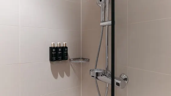 Moderni suihku beigellä laatoituksella, jossa suihkupää, hana ja seinäpullot: suihkugeeli, shampoo ja hoitoaine.