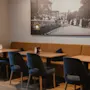 Et komfortabelt restaurantområde med træborde, mørke stole og en lang brun bås, under et stort vægbillede.