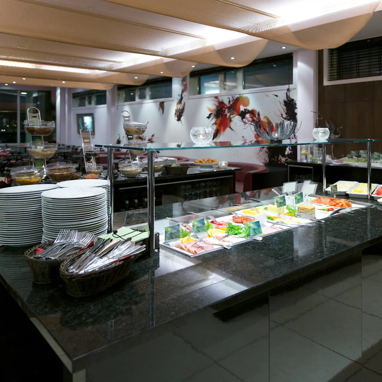 Buffet tables with various foods and utensils, set in a well-lit, contemporary dining room.