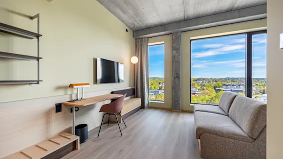 A bright, modern room with a dedicated workspace, comfortable sofa, and expansive windows overlooking a vibrant landscape.