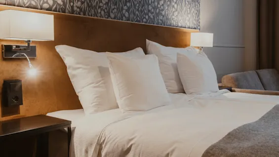 Ett mysigt hotellrum med en prydligt bäddad säng med vita lakan, mjuk belysning och en bekväm atmosfär.