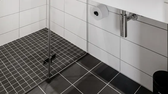 Et moderne baderom med dusjkabinett i glass, hvite fliser og et veggmontert servant med toalettsaker.