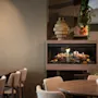 Viihtyisä ravintola- tai lounge-alue, jossa on moderni takka, pöytiä, tuoleja ja sytytettyjä kynttilöitä, luoden lämpimän ja kutsuvan tunnelman.