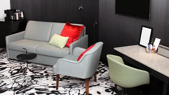 A modern living area with a grey sofa, colored pillows, armchairs, and a flat-screen TV, in a dark-walled room with patterned carpet.