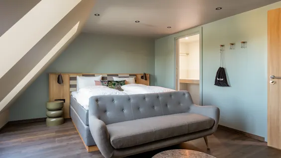 Et moderne og hyggeligt hotelværelse med en seng, en grå sofa og et lille bord. 