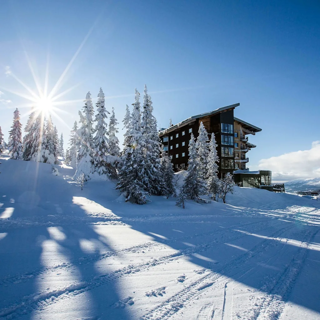 Sunny winter day at Copperhill Mountain Lodge in Åre, with a hotel building, snow-covered trees, and ski tracks.