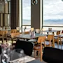En lys restaurant på Quality Hotel Harstad med bord dekket for bespisning, med utsikt over vann og fjell.