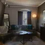 A cozy living room features a grey sofa with blue cushions and a side chair, complemented by a round coffee table. A floor lamp and framed pictures enhance the warm, inviting ambiance.