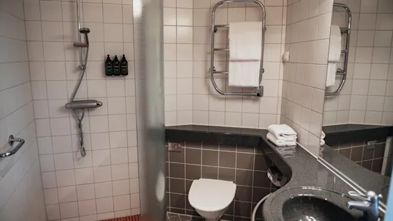 A contemporary bathroom at Home Hotel Uppsala, offering a refreshing shower, toilet, and sink area with neatly folded towels.