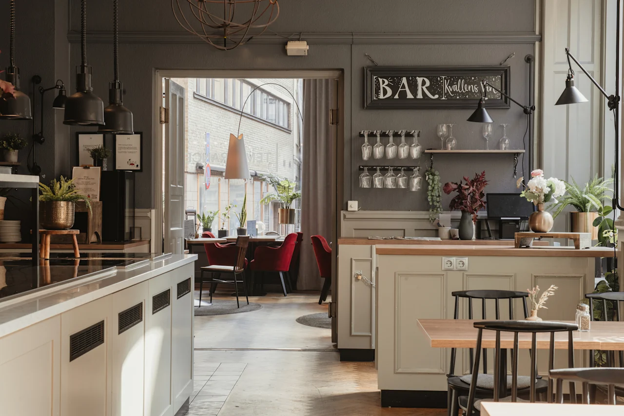 Et koselig bar- og restaurantinteriør med et skilt hvor det står BAR, som fører til et uteserveringsområde på en solrik dag.