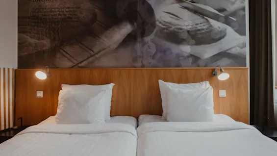 Two inviting beds with white linens in a hotel room at Home Hotel Uppsala. A wooden headboard and a mural with the word BAGARE.