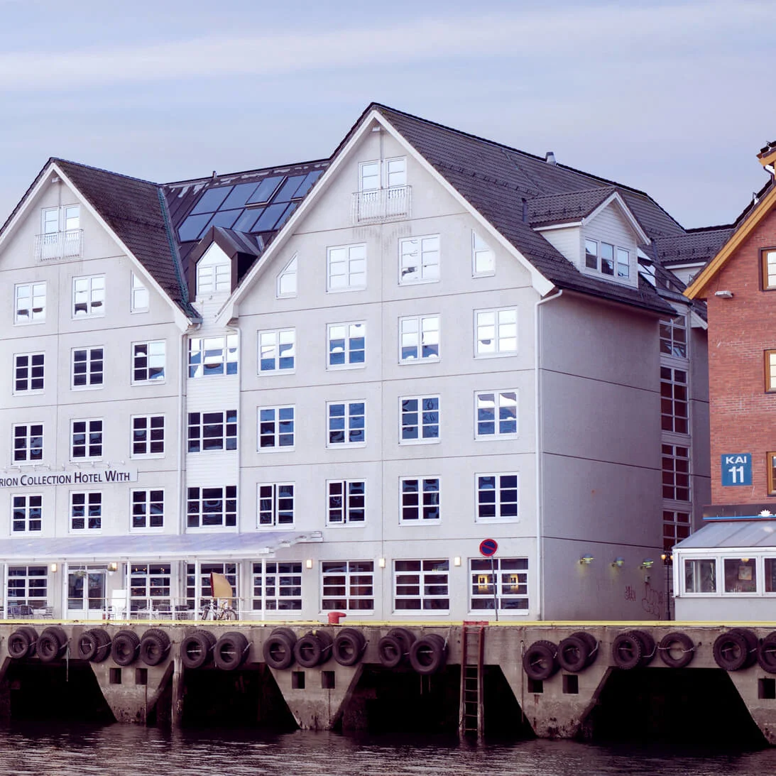 Traditionelle bygninger på en havnekaj med skiltet "Home Hotel With" imod en tusmørkehimmel.