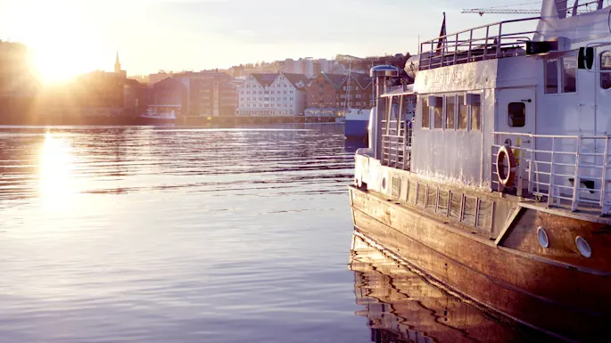 Moored boat at sunset, golden light reflecting on calm water, cityscape in the background.
