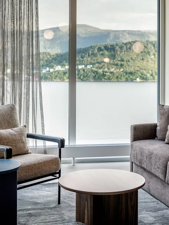 Et komfortabelt oppholdsrom med sofa og lenestol, som tilbyr en naturskjønn utsikt over vann og fjell.