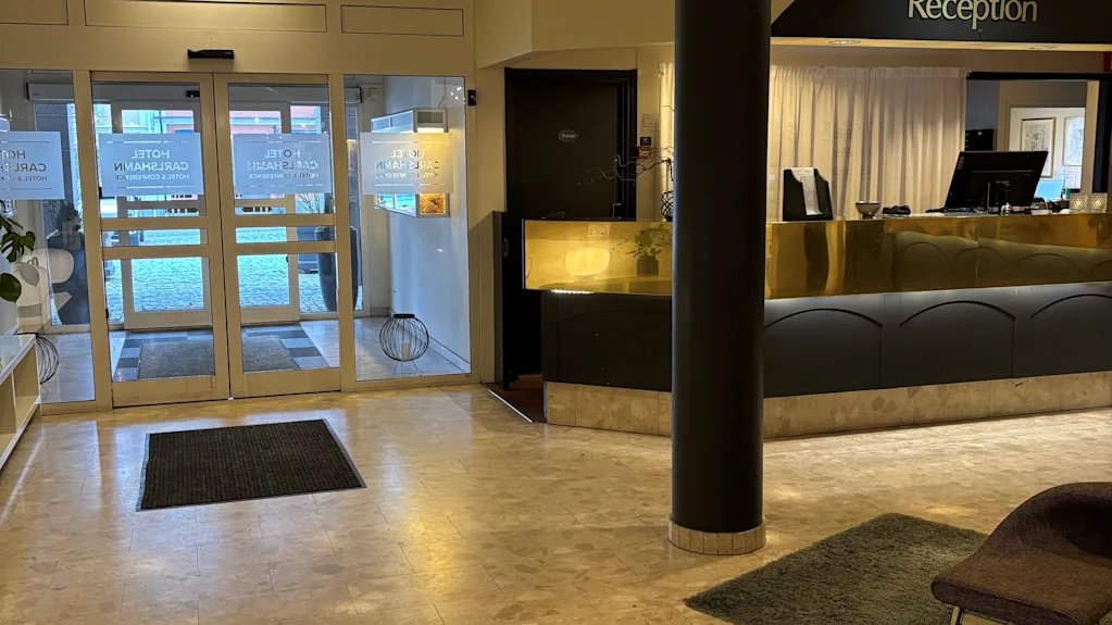 Ljus hotellobby med en reception och entredorrar i glas