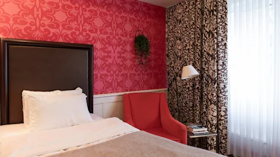 A cozy hotel room at Home Hotel Grand Bodø with a single bed, a red armchair, and vibrant patterned wallpaper.