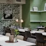 Moderna café med snyggt arrangerade bord och stolar, dekorerade med botanisk tapet och gröna väggar. Svartvitt tigerfotografi och stadslandskapskonstverk ger en visuell intresse till den avslappnade atmosfären.