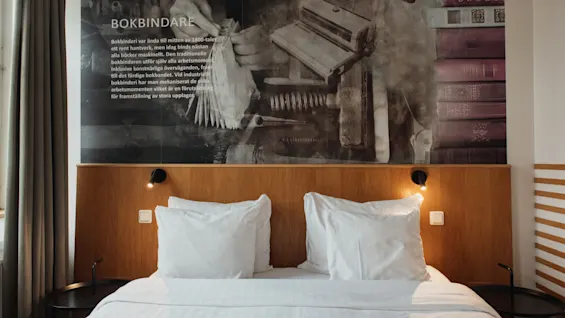 Home Hotel Uppsala room with a bed and a mural featuring bookbinding tools and text BOKBINDARE.