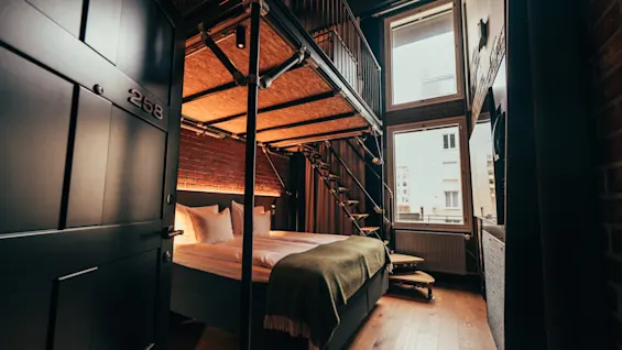 A stylish hotel room with a loft bed, exposed brick, and large windows, offering a modern and comfortable stay. Room 258.