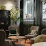A cozy lounge area at Home Hotel Uppsala with comfortable armchairs, a coffee table, a bookshelf, and lush green plants.