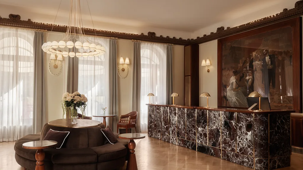 Den eleganta lobbyn på Hotel Kämp med en receptionsdisk i mörk marmor, en cirkulär sittgrupp och en stor ljuskrona.