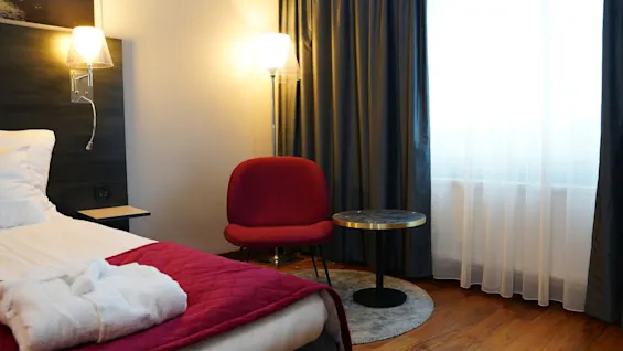 Viihtyisä hotellihuone Quality Hotel Sundsvallissa sängyllä, punaisella nojatuolilla ja ikkunalla, valmiina rentouttavaan oleskeluun.