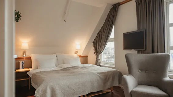 A cozy hotel room with a comfortable bed, an armchair, and a TV, perfect for relaxation.