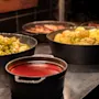 En varm buffé med ulike retter i svarte gryter, inkludert dampede grønnsaker, poteter med urter og en fyldig rød saus.