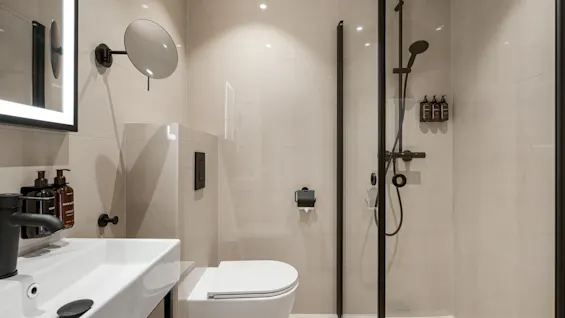 Et moderne badeværelse med hvid håndvask, toilet og en bruser med elegante sorte armaturer. Neutrale toner og rent design.