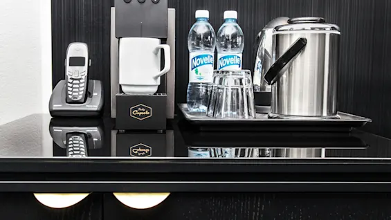A coffee machine with a mug beneath, next to bottled water and a kettle, on a glossy black countertop against a dark wall.