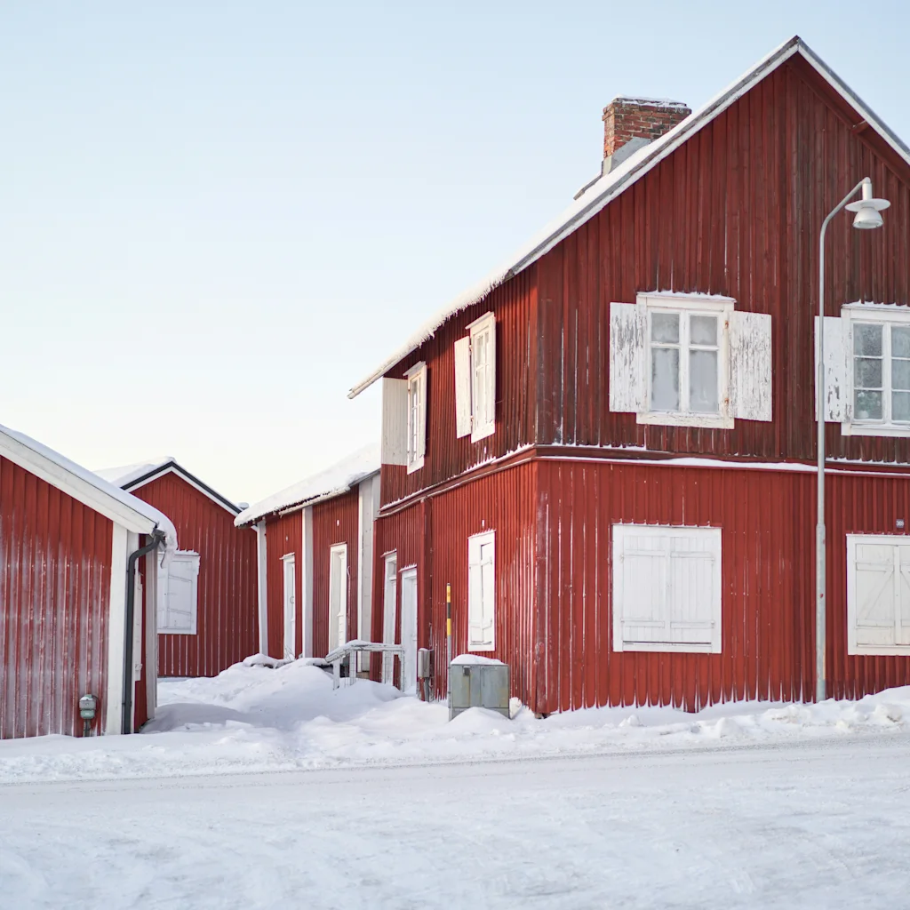Røde træhuse med hvide skodder i sneklædte Gammelstad Kyrkstad i Luleå. Gadeskiltet Framlänningsvägen er synligt.