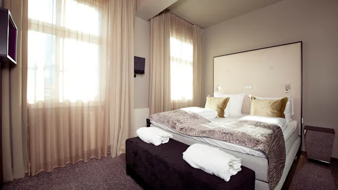 A neatly made bed with pillows in a sunlit, tidy bedroom.
