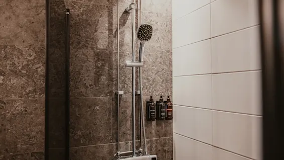 Siisti ja moderni suihkutila tummilla ja valkoisilla laatoitetuilla seinillä, jossa on suihkupää ja seinään kiinnitetyt hygieniatuotteet.