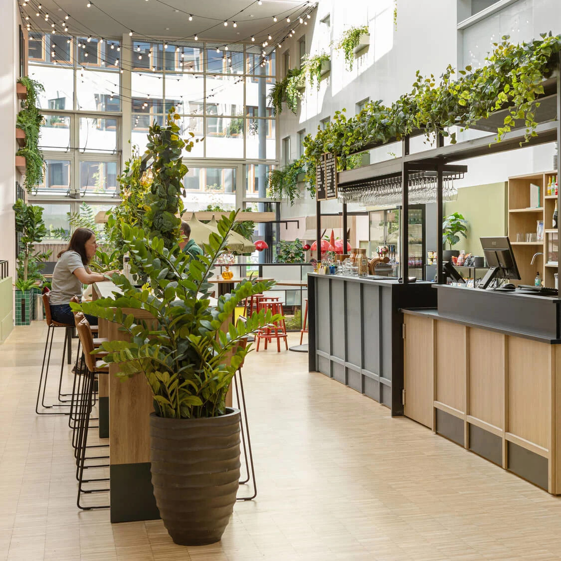 Barbord med överhängande grönska, en anställd vid kassan och en neonskylt som säger "BARCEPTION". Inomhusmiljö med växter och sittplatser i bakgrunden.