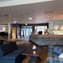 Resepsjonsdisk med steinfront og en bartender som forbereder drinker, plassert i en moderne salong med komfortable sitteplasser, tregulv og stemningsbelysning.