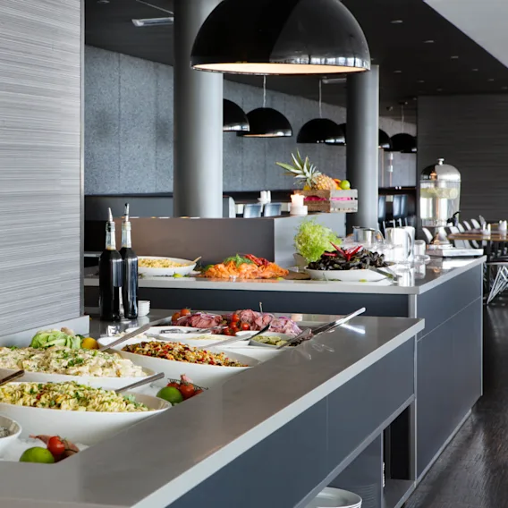 Buffébord som viser forskjellige salater og retter, pyntet med friske grønnsaker og urter. Miljøet er en moderne restaurant med store, svarte pendellamper.