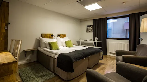A neatly made bed with green accents in a modern bedroom, two armchairs in the foreground.