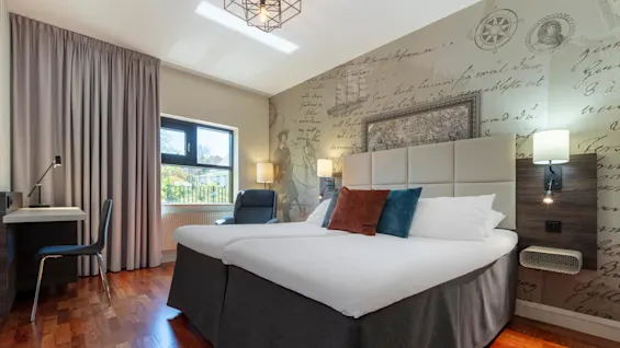 Modern bedroom with a king-size bed, patterned feature wall, and wooden floor, showcasing furniture and a window with daylight.