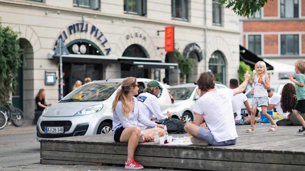 People relaxing and children playing on a sunny day, with a pizza restaurant in the background. Sønder Boulevard on Vesterbro in Copenhagen.