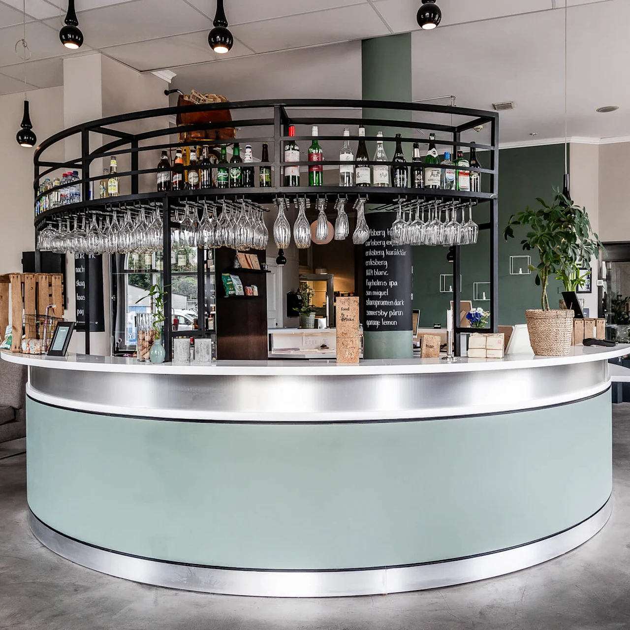 A curved bar with bottles and glasses, in a cozy cafe setting with sofas and framed pictures on the walls.