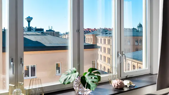 A clear day viewed through an open window, with city buildings and blue sky.