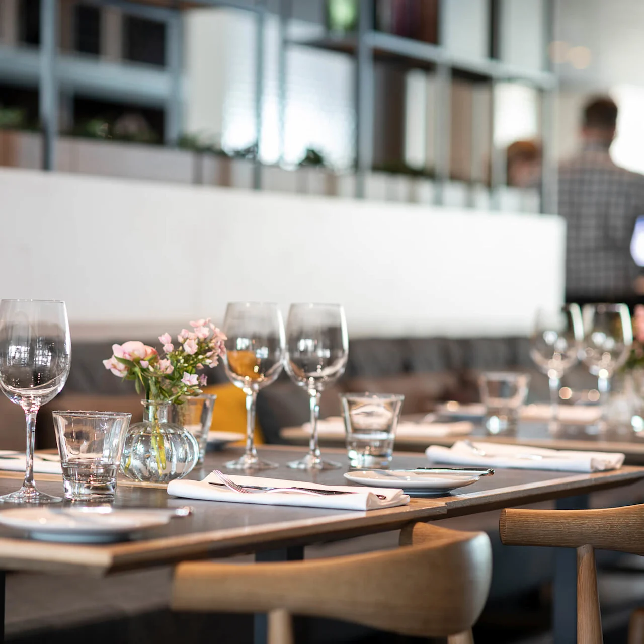 Elegant table setting with empty wine glasses and flowers; arranged on a wooden table in a modern restaurant with cushioned seating and a partitioned backdrop.