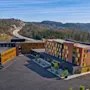 En moderne hotellbygning med en stor parkeringsplass, mot et bakteppe av skogkledde åser og en svingete vei.