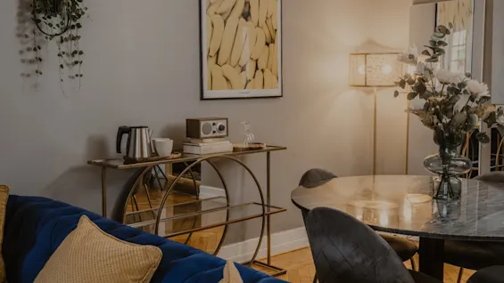 En elegant och bekväm hotellvardagsrumsdel med en blå soffa, ett matbord och en gyllene konsol, vilket skapar en välkomnande atmosfär.