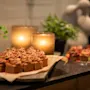 Sjokolademuffins med virvlet glasur hviler på et fat. To tente stearinlys og potteplanter pynter den mørke overflaten, og skaper en varm, innbydende atmosfære.