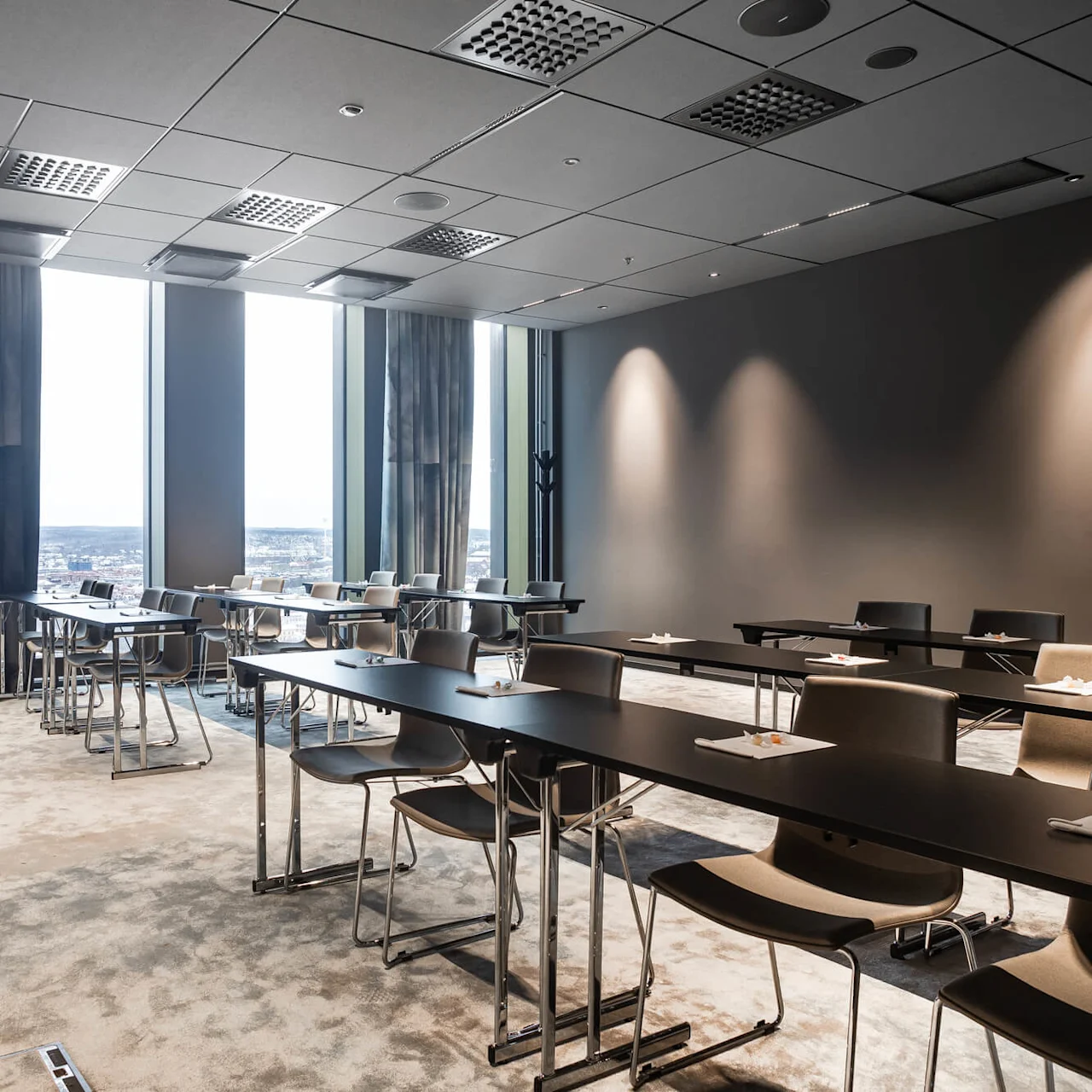Konferensrum med bord dukade för ett möte, innehållande anteckningsblock och pennor, mot stora fönster med stadsvy; solljus lyser upp det moderna, minimalistiska inredningen.